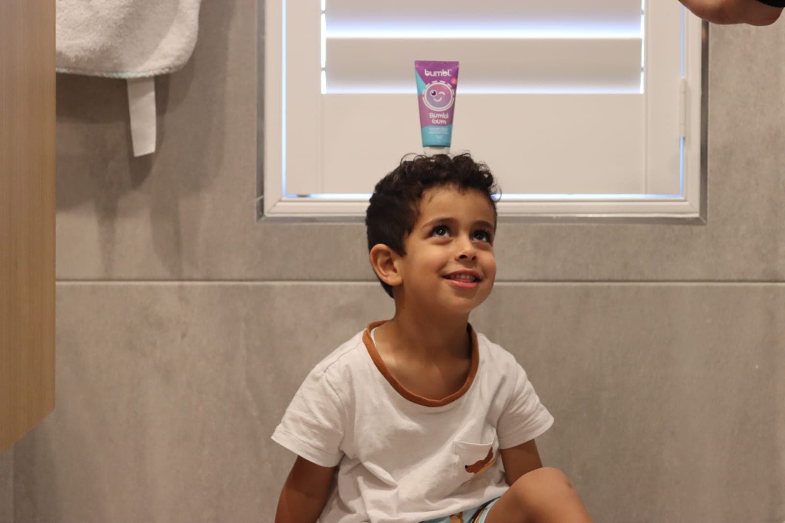 A boy in the bathroom balancing a Bumbl Co tube on his head at brushing time
