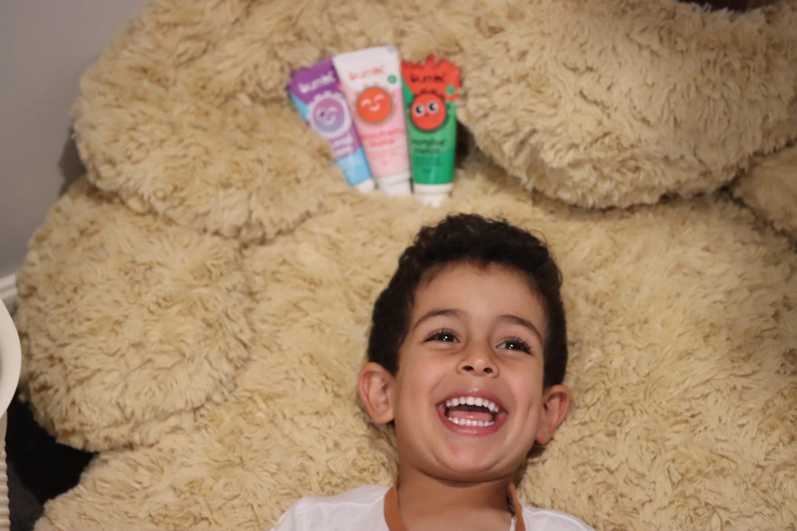 A laughing boy in front of all three Bumbl Co flavours lined up on a giant teddy