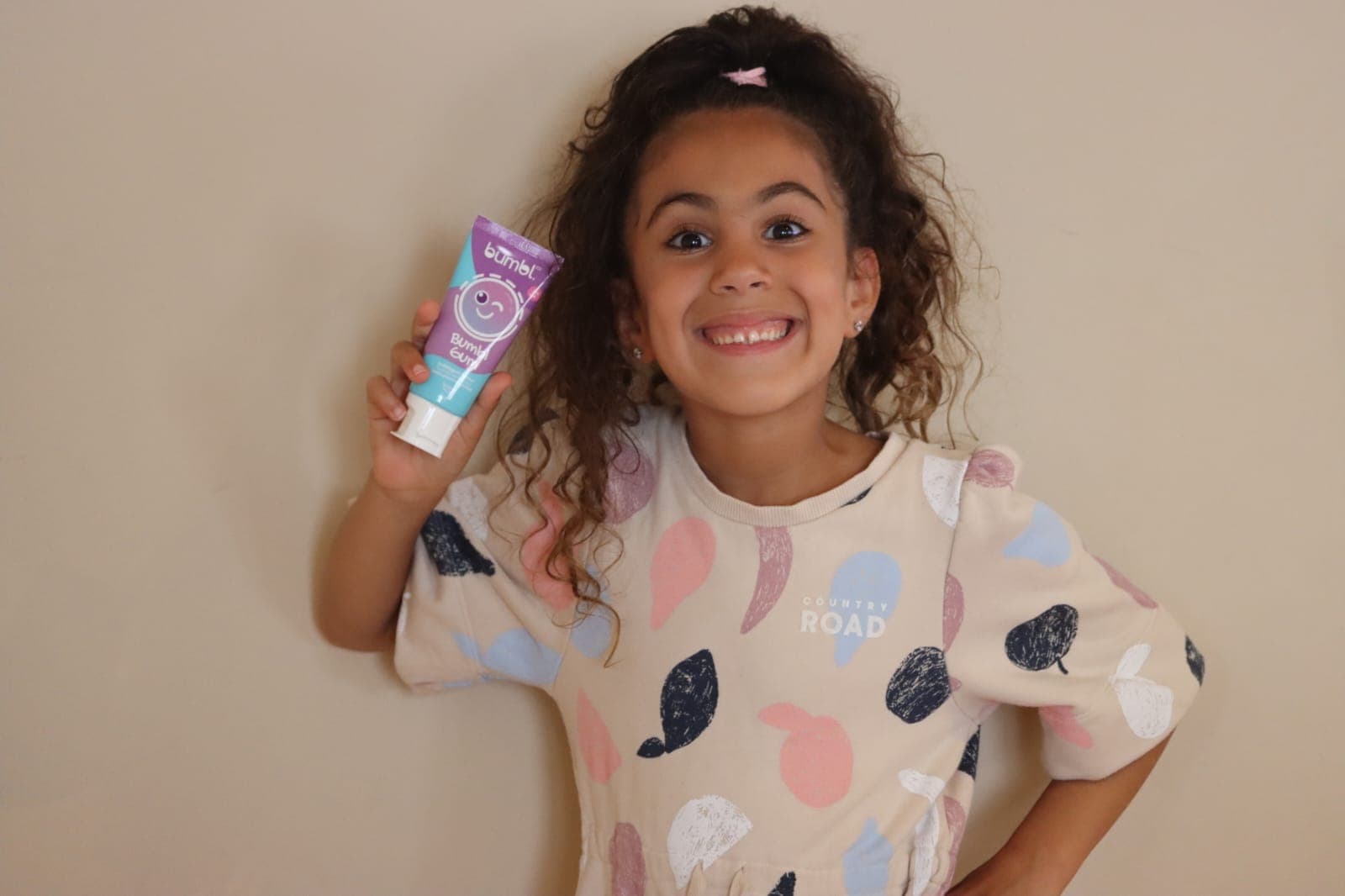 A smiling girl holding a Bumbl Gum tube of Bumbl Co toothpaste